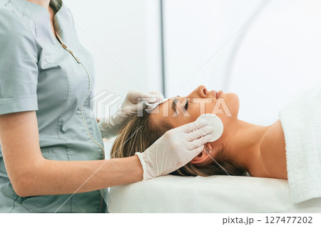 Side view. Woman face getting facial care by beautician hands at spa salon Side view. Woman face getting facial care by beautician hands at spa salon 127477202