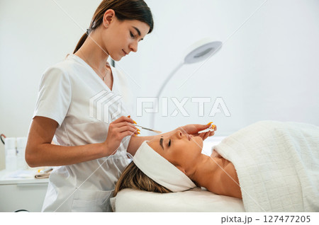 Woman face getting facial care by beautician hands at spa salon Woman face getting facial care by beautician hands at spa salon 127477205