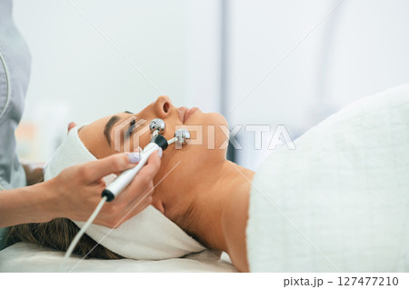 Professional equipment. Woman face getting facial care by beautician hands at spa salon 127477210