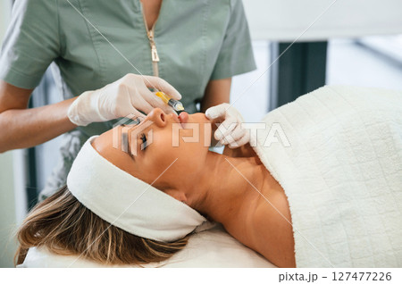 A rejuvenating shot. Woman face getting facial care by beautician hands at spa salon A rejuvenating shot. Woman face getting facial care by beautician hands at spa salon 127477226