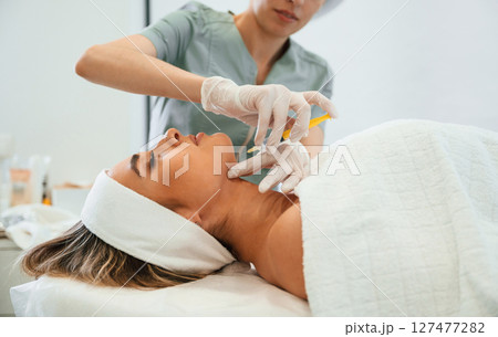 Yellow colored syringe, making injection. Woman face getting facial care by beautician hands at spa salon Yellow colored syringe, making injection. Woman face getting facial care by beautician hands at spa salon 127477282