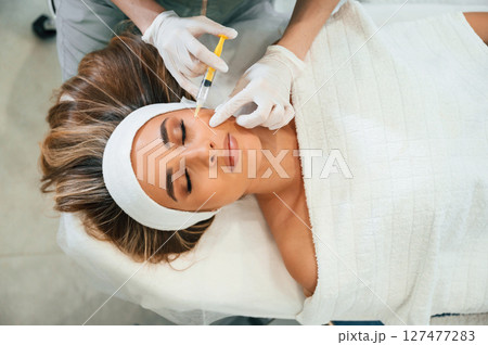 Injection into the face skin. Woman face getting facial care by beautician hands at spa salon 127477283