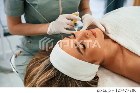 Injection into the face skin. Woman face getting facial care by beautician hands at spa salon 127477286