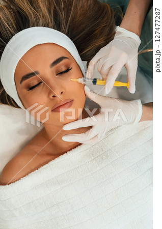 Injection into the face skin. Woman face getting facial care by beautician hands at spa salon Injection into the face skin. Woman face getting facial care by beautician hands at spa salon 127477287