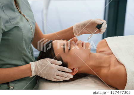 Putting liquid on lips. Woman face getting facial care by beautician hands at spa salon 127477303
