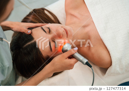 Electrical therapy tool. Woman face getting facial care by beautician hands at spa salon 127477314