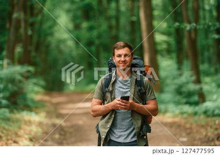 Big backpack and smartphone. Tourist in summer forest. Conception of exploration and leisure Big backpack and smartphone. Tourist in summer forest. Conception of exploration and leisure 127477595