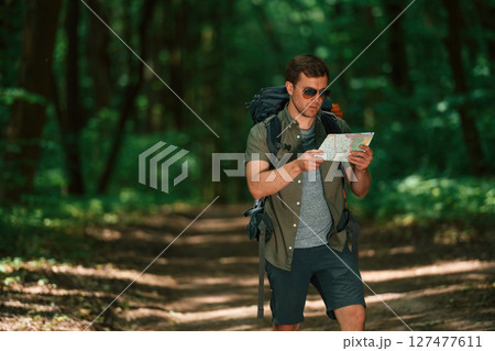 Holding the map. Tourist in summer forest. Conception of exploration and leisure Holding the map. Tourist in summer forest. Conception of exploration and leisure 127477611