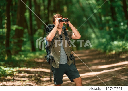 Looking through the binoculars. Tourist in summer forest. Conception of exploration and leisure Looking through the binoculars. Tourist in summer forest. Conception of exploration and leisure 127477614
