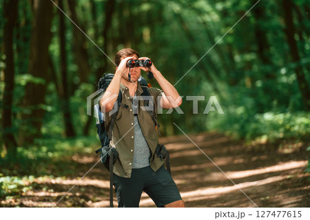 Looking through the binoculars. Tourist in summer forest. Conception of exploration and leisure Looking through the binoculars. Tourist in summer forest. Conception of exploration and leisure 127477615