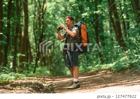 Standing and holding binoculars. Tourist in summer forest. Conception of exploration and leisure 127477622