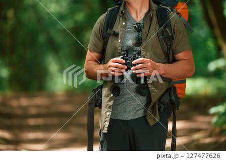 Holds binoculars. Close up view of tourist that is in summer forest Holds binoculars. Close up view of tourist that is in summer forest 127477626