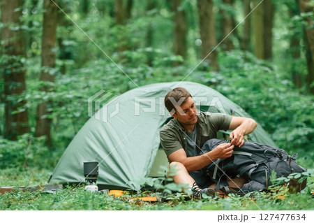 Green colored tent is behind. Tourist in summer forest. Conception of exploration and leisure 127477634