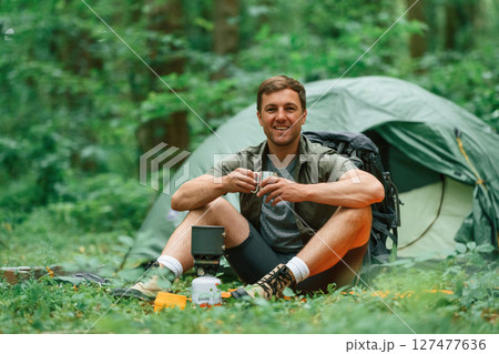 Boiling water, sitting near the tent. Tourist in summer forest. Conception of exploration and leisure 127477636