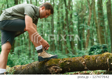 Standing and ties shoelaces. Tourist in summer forest. Conception of exploration and leisure 127477642