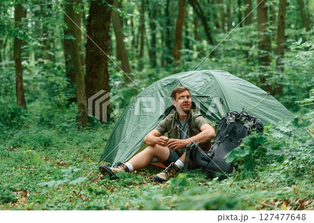 With cup of water. Sitting near the tent. Tourist in summer forest. Conception of exploration and leisure 127477648