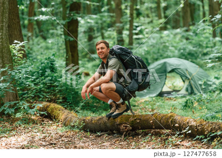 Sitting on the fallen tree. Tourist in summer forest. Conception of exploration and leisure Sitting on the fallen tree. Tourist in summer forest. Conception of exploration and leisure 127477658