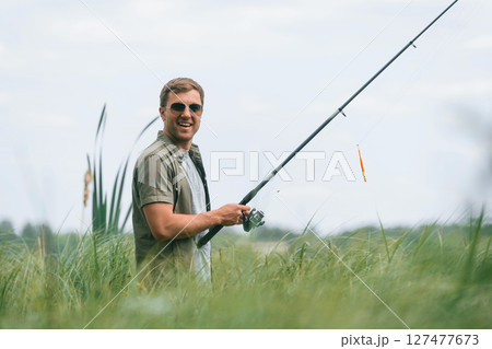 Positive and handsome man in sunglasses is fishing outdoors Positive and handsome man in sunglasses is fishing outdoors 127477673