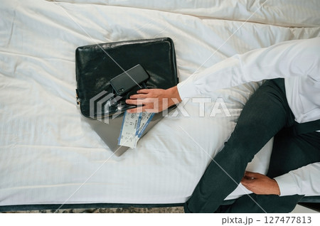 Close up view of businessman that is sitting on bed with tickets for travel on it 127477813