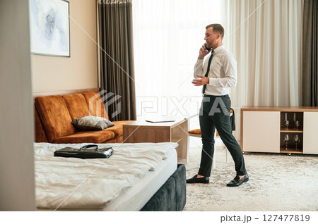 Phone conversation. Businessman is indoors in the hotel room 127477819
