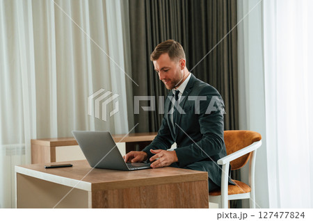 In the office with laptop. Handsome businessman is indoors in the hotel room In the office with laptop. Handsome businessman is indoors in the hotel room 127477824
