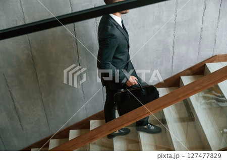 Walking up. Man in business suit and tie with case in hands is on the stairs 127477829