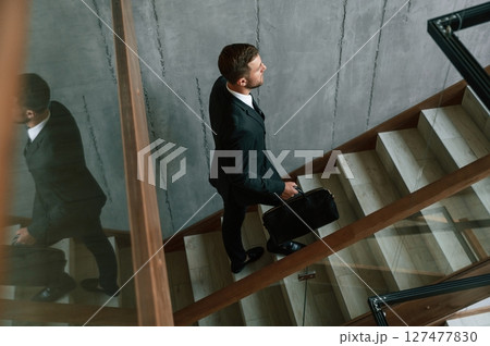 Walking up. Man in business suit and tie with case in hands is on the stairs 127477830