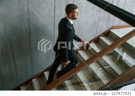 Walking up. Man in business suit and tie with case in hands is on the stairs 127477831