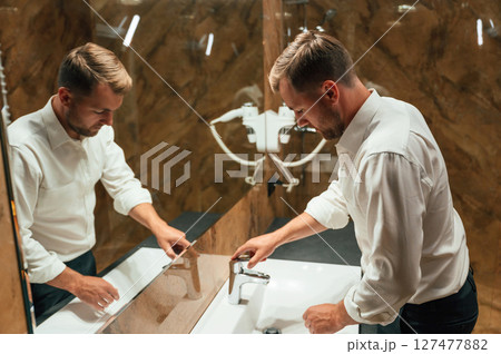Washing hands. Man in formal clothes is in the bathroom against mirror 127477882