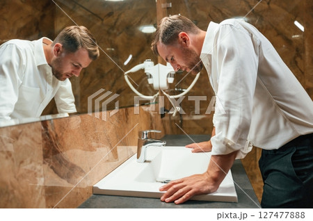 Man in formal clothes is in the bathroom against mirror Man in formal clothes is in the bathroom against mirror 127477888