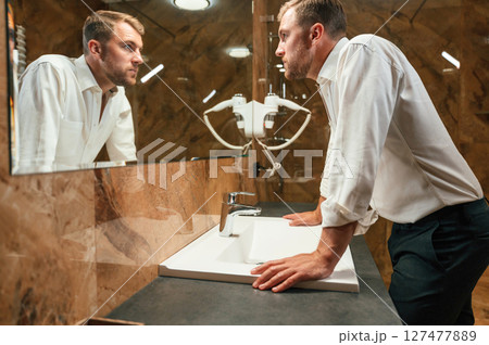 Man in formal clothes is in the bathroom against mirror Man in formal clothes is in the bathroom against mirror 127477889