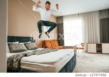 Jumping on the bed. Businessman is indoors in the hotel room Jumping on the bed. Businessman is indoors in the hotel room 127477898
