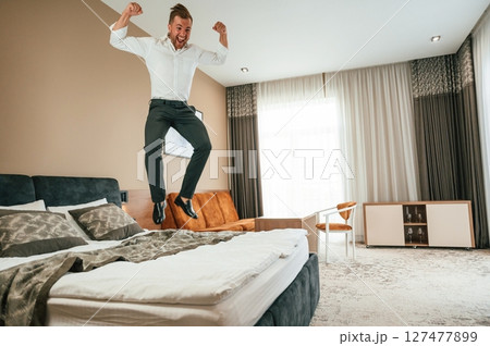 Jumping on the bed. Businessman is indoors in the hotel room 127477899