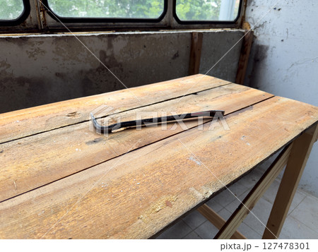 Rusty pry bar lying on a rough wooden workbench in a partially renovated room. The old peeling wall and dusty windows add a gritty, authentic construction site atmosphere 127478301