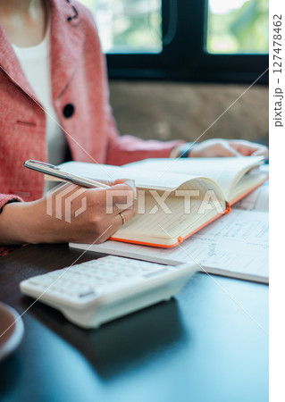 A business professional takes notes in a planner with a calculator on the desk, capturing a moment of productivity in a modern office. A business professional takes notes in a planner with a calculator on the desk, capturing a moment of productivity in a modern office. 127478462