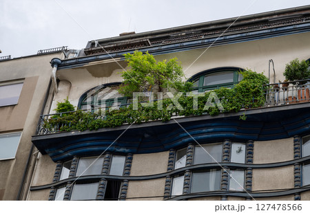 Ornate residential building facade with curved balcony, green plants, and arched windows  127478566