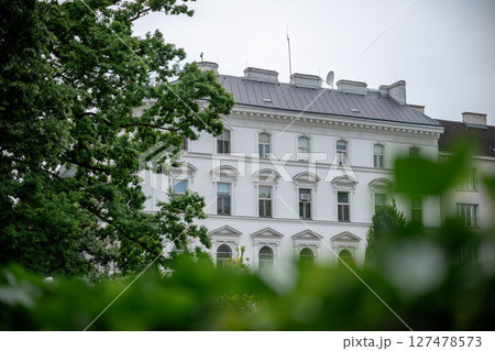 White historic building with arched windows behind green tree foliage in daylight White historic building with arched windows behind green tree foliage in daylight 127478573