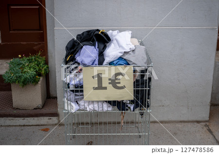 Used clothing in a metal crate with a 1 euro sign, placed outdoors, concept of thrift shopping Used clothing in a metal crate with a 1 euro sign, placed outdoors, concept of thrift shopping 127478586