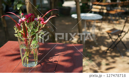 Colorful flowers in a glass vase adorn a wooden table in a serene outdoor setting Colorful flowers in a glass vase adorn a wooden table in a serene outdoor setting 127478718