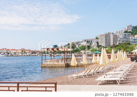 Empty sun loungers and closed umbrellas on the Adriatic coast. Summer beach infrastructure and seaside tourism in Budva, Montenegro Empty sun loungers and closed umbrellas on the Adriatic coast. Summer beach infrastructure and seaside tourism in Budva, Montenegro 127481098