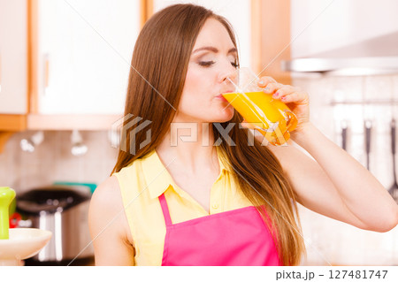 Woman in kitchen drinking fresh orange juice 127481747