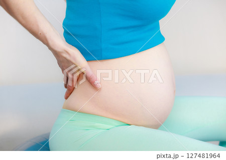 Pregnant woman sitting on couch holds hand on her back 127481964