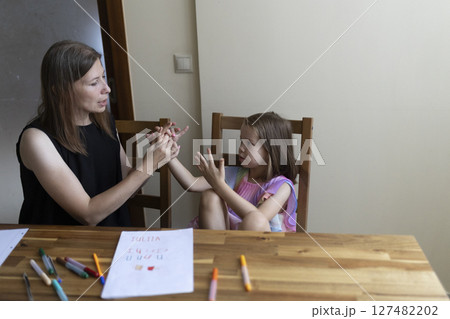 Teacher helping young girl learning sign language at home 127482202