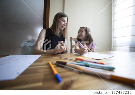Mother helping daughter drawing with colored markers at home 127482230