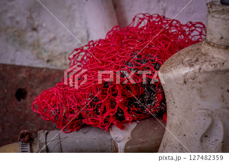 Tangled red netting discarded on a dirty pipe surface 127482359