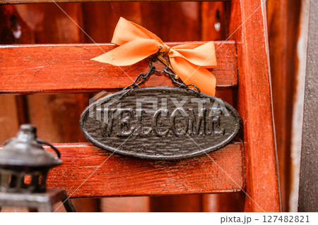 Rustic welcome sign with orange ribbon on wooden background. Home decor, hospitality greeting, and cozy entrance details. 127482821