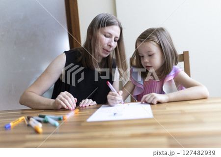 Babysitter helping little girl with homework, drawing with felt-tip pens Babysitter helping little girl with homework, drawing with felt-tip pens 127482939