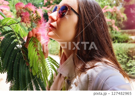 Beautiful girl smelling Chinese acacia pink flowers Young woman in spring garden 127482965