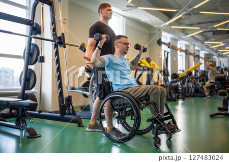 Personal coach guides disabled athlete in gym. Workout post injury recovery, mobility adaptation 127483024
