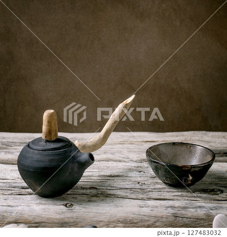 Original handmade ceramic teapot with wooden handle and cups for traditional Chinese tea drinking on an old wooden table. Decorative sea pebbles all around. Copy space Original handmade ceramic teapot with wooden handle and cups for traditional Chinese tea drinking on an old wooden table. Decorative sea pebbles all around. Copy space 127483032